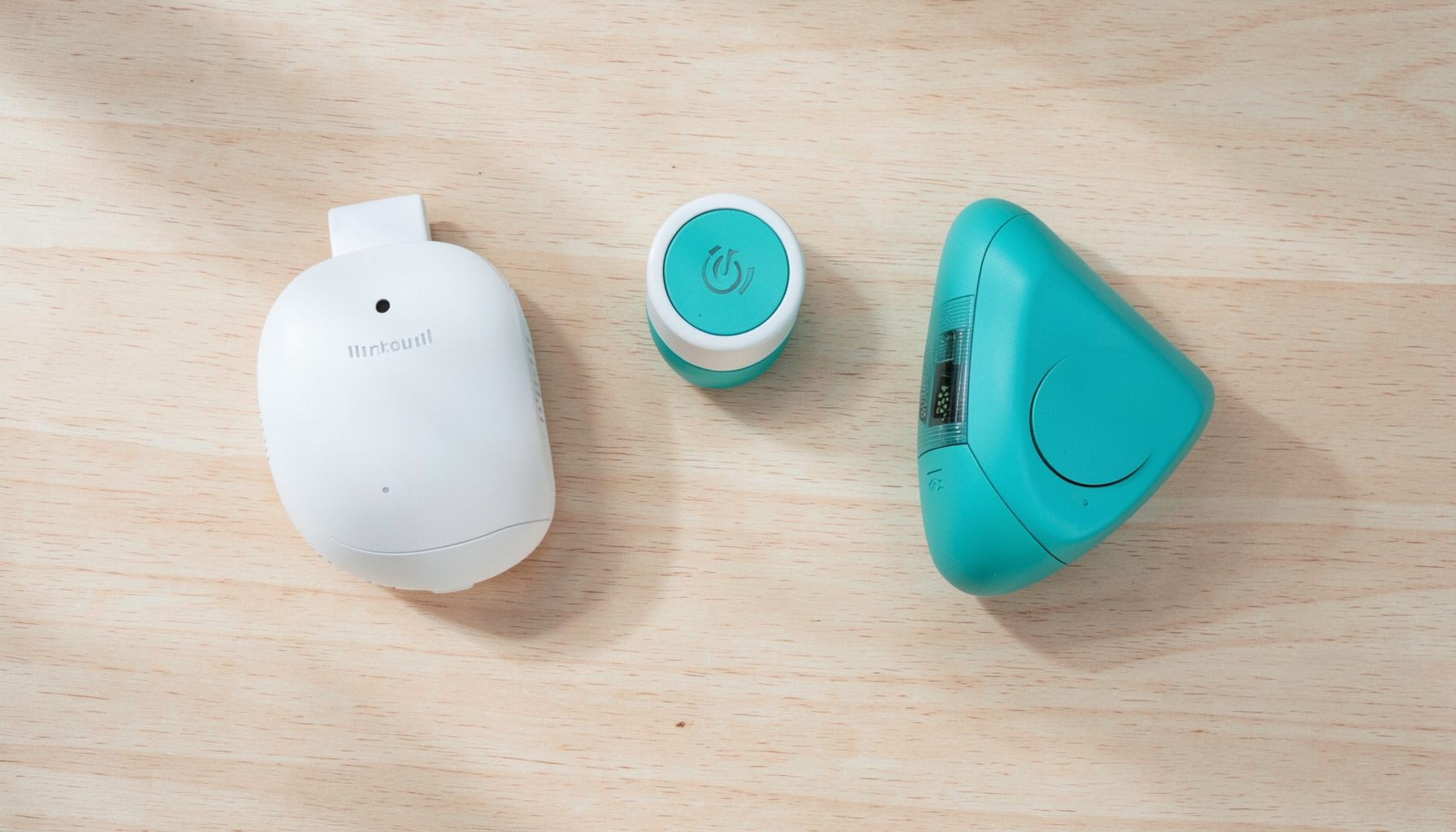 Overhead flat-lay photograph of smart home devices including a smart plug, wireless contact sensor, and thermometer sensor arranged on a light wooden surface with soft natural shadows