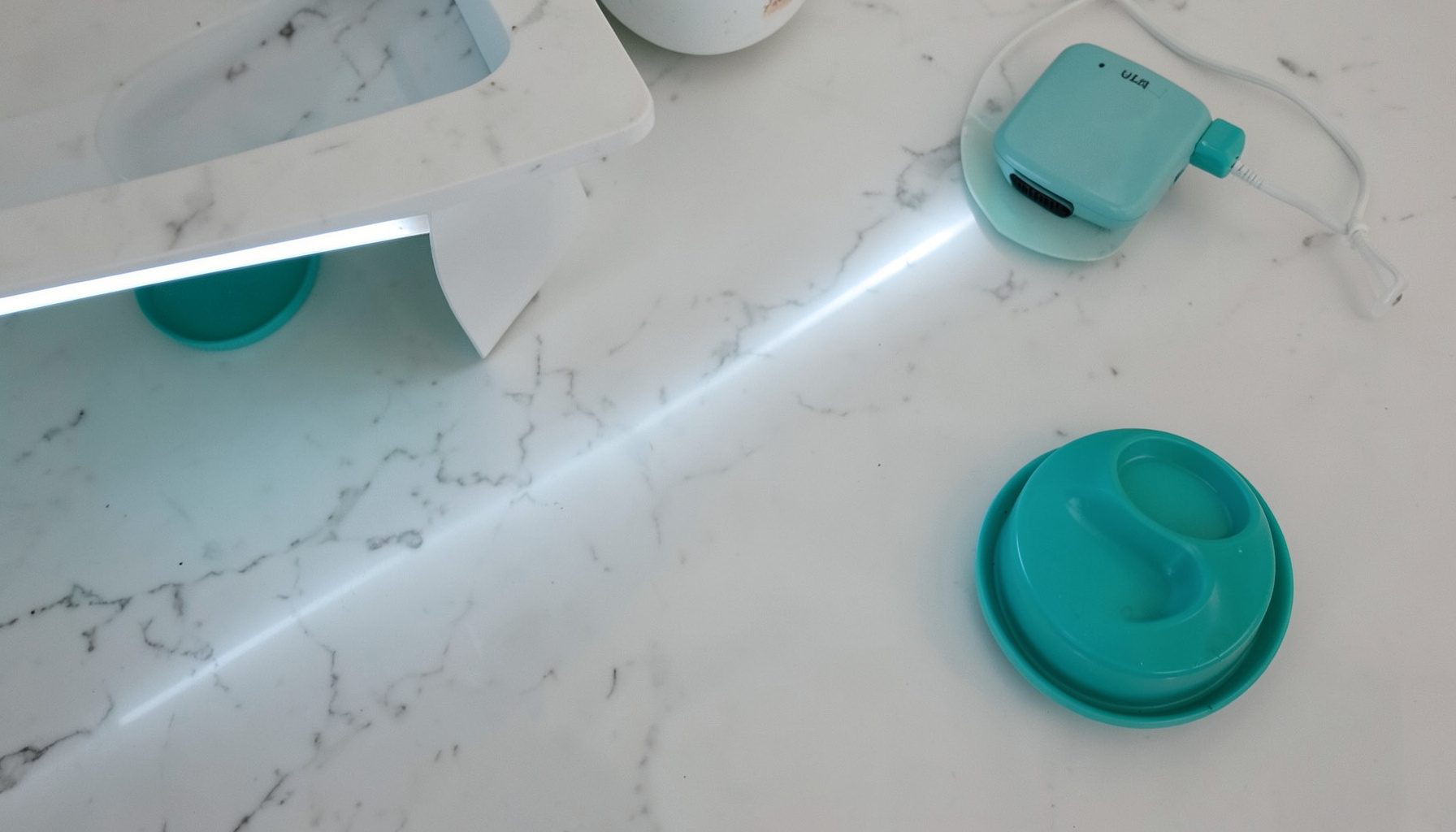 A sleek LED light strip running along the underside of a kitchen cabinet, illuminating a marble countertop in cool white