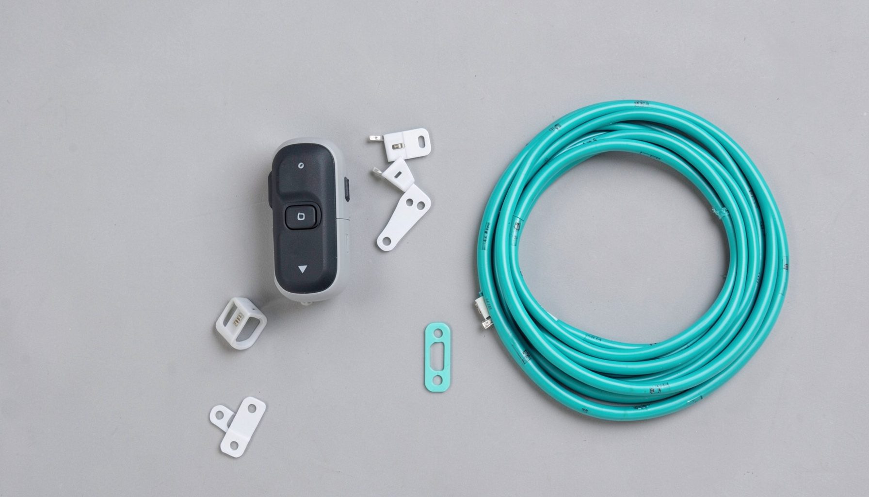 A small remote control and a set of mounting clips arranged beside a coiled LED strip on a neutral grey background