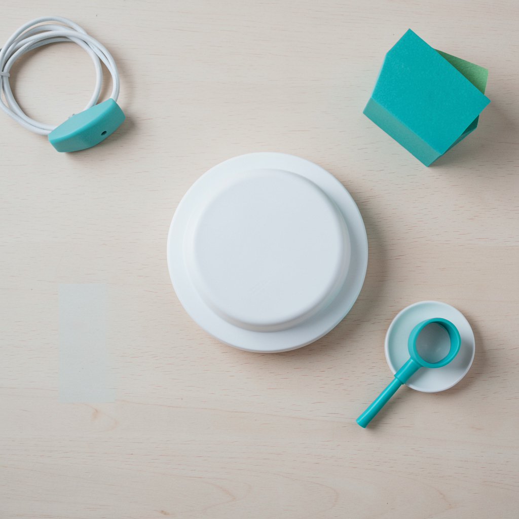 Overhead flat-lay photograph of a minimalist round ceiling light fixture on a light wooden surface, soft neutral tones