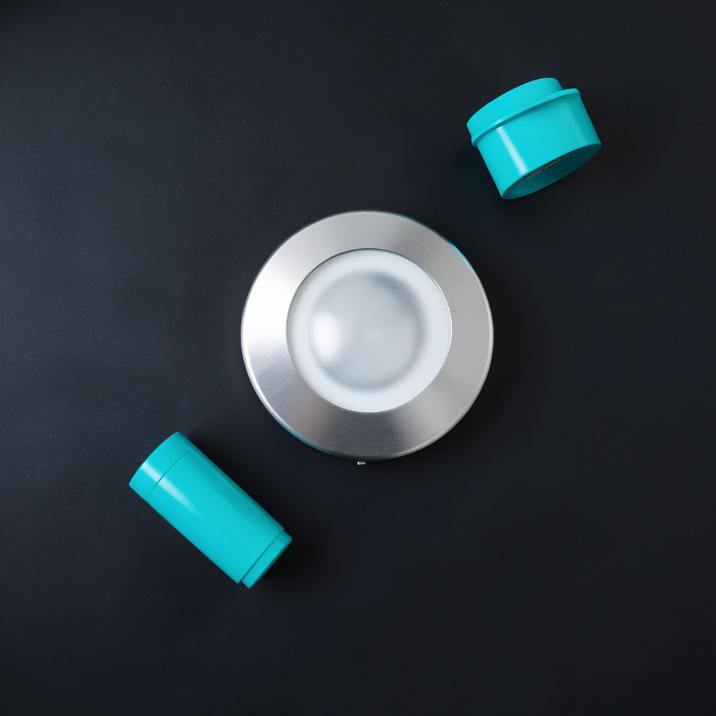 Overhead flat-lay photograph of a semi-flush ceiling light with brushed metal accents on a dark matte surface