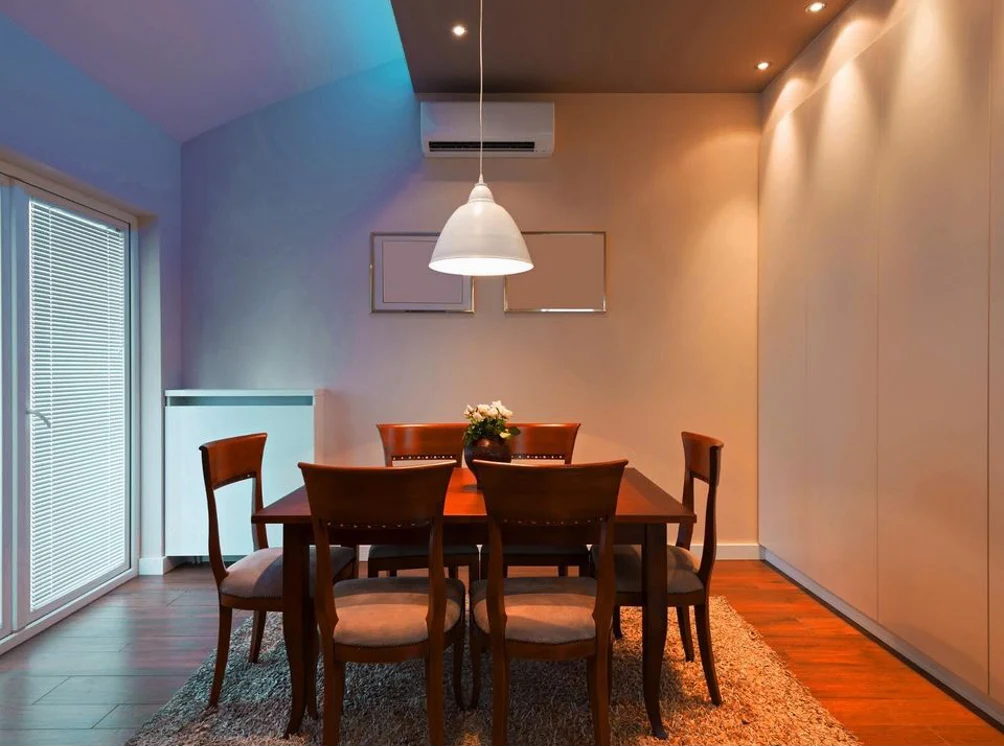 Dining room with a wooden table and chairs, a pendant lamp overhead and a wall-mounted unit, mixing warm and cool light