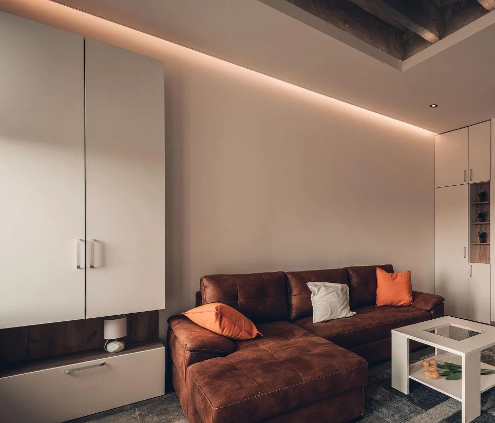 Cosy living room with a brown leather sectional sofa, orange and white cushions and warm strip lighting along the cabinetry